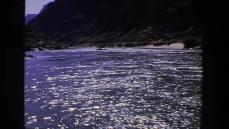 1969 Utah home-movie frame of sparkling blue river water leading toward a rugged canyon shoreline and dark mountain slopes.