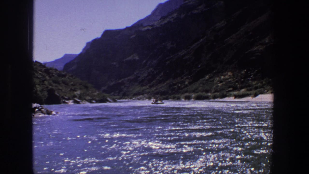 River running between steep canyon walls with bright reflections and distant boats.