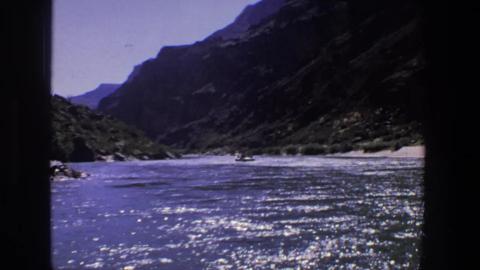1969 Utah 8mm frame showing a broad river, steep rocky canyon walls, bright surface glare, and small distant boats.