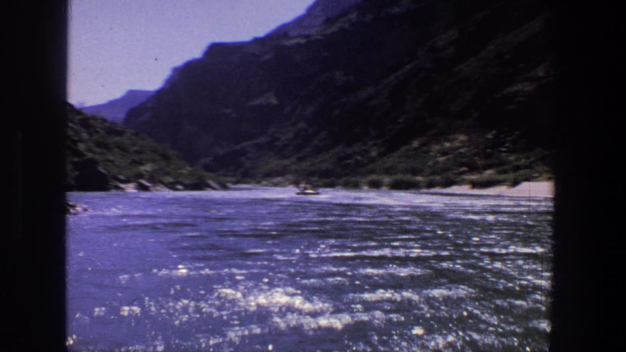 Wide river view with rugged canyon slopes, shoreline vegetation, and small boats in the distance.