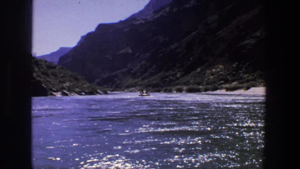 1969 Utah 8mm frame showing reflective river water, steep canyon walls, shoreline greenery, and a small distant boat.