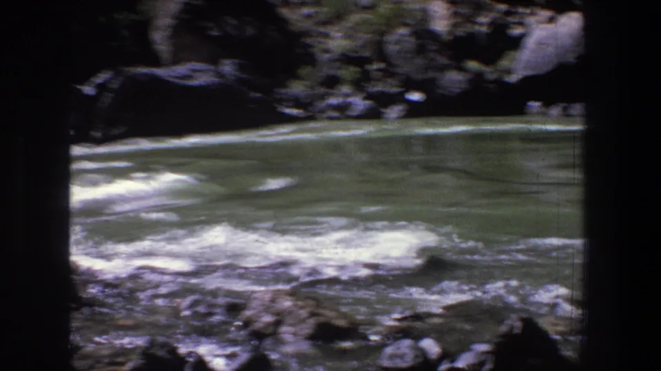 1969 Utah canyon river footage frame with whitewater, dark rocks, and green water moving through the channel.
