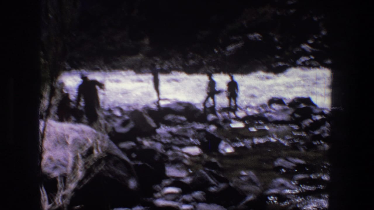 1969 Utah 8mm frame showing silhouetted figures on rocks near a fast stream, partly obscured by dark trees.