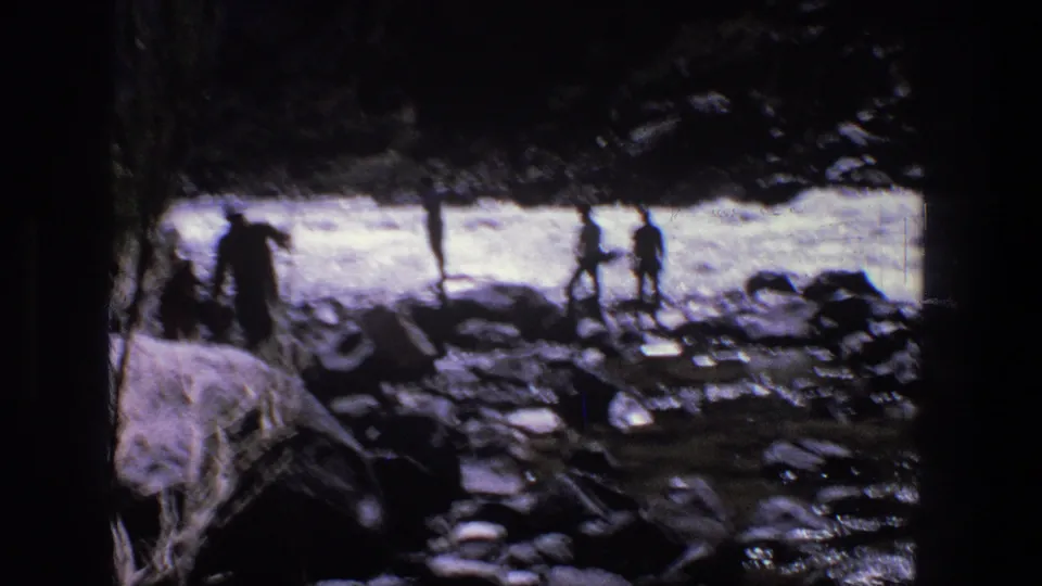1969 Utah 8mm frame showing silhouetted figures on rocks near a fast stream, partly obscured by dark trees.
