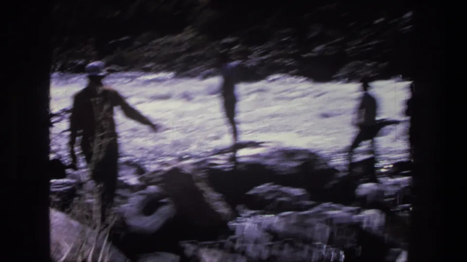 1969 Utah home-movie frame with a dark figure near rocky streamside terrain and bright water in the background.