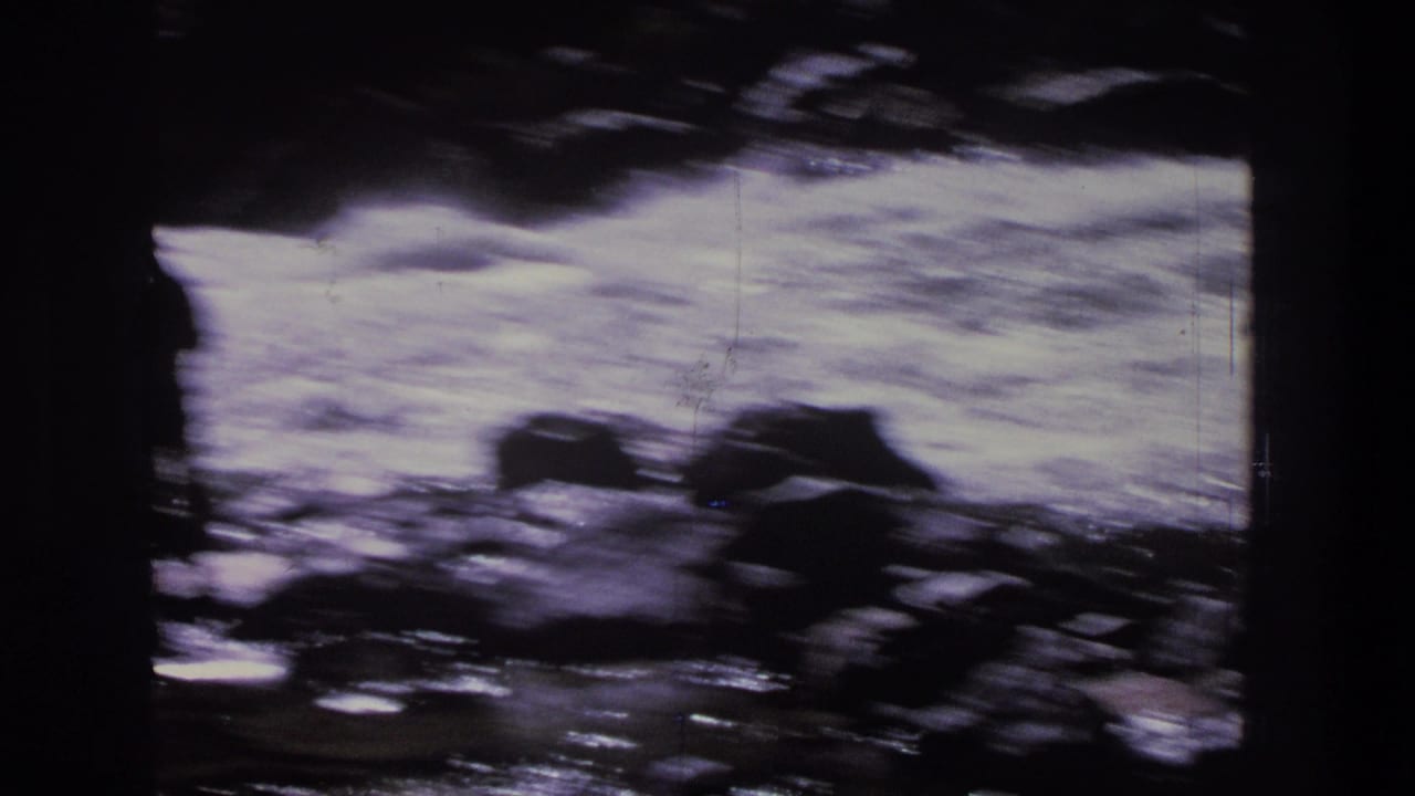 Foamy river rapids with dark rocks and a blurred raft near the water.