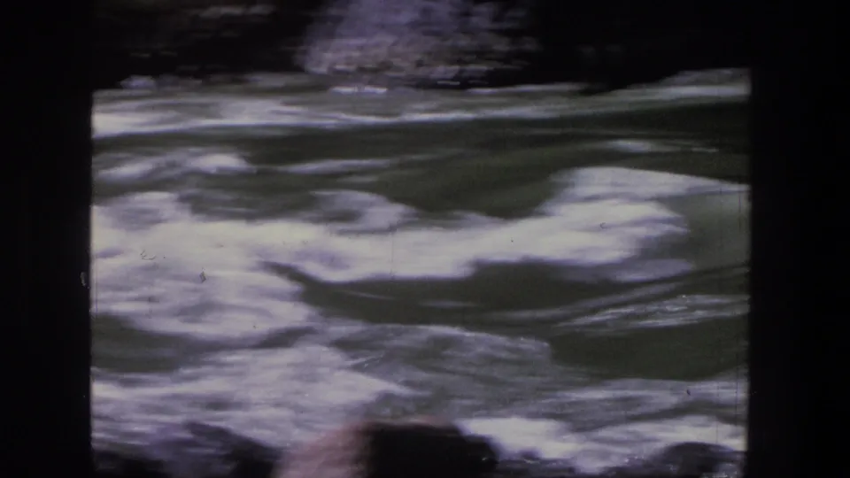 Handheld 8mm view of Utah rapids, with foamy current, dark shoreline rocks, and a partially visible raft near the lower frame.