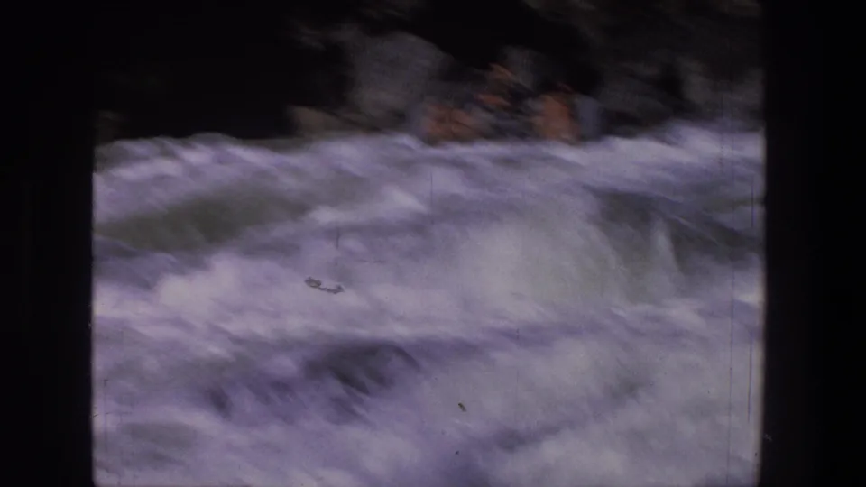1969 Utah home-movie frame showing a raft and indistinct riders amid heavy whitewater and dark rocks.
