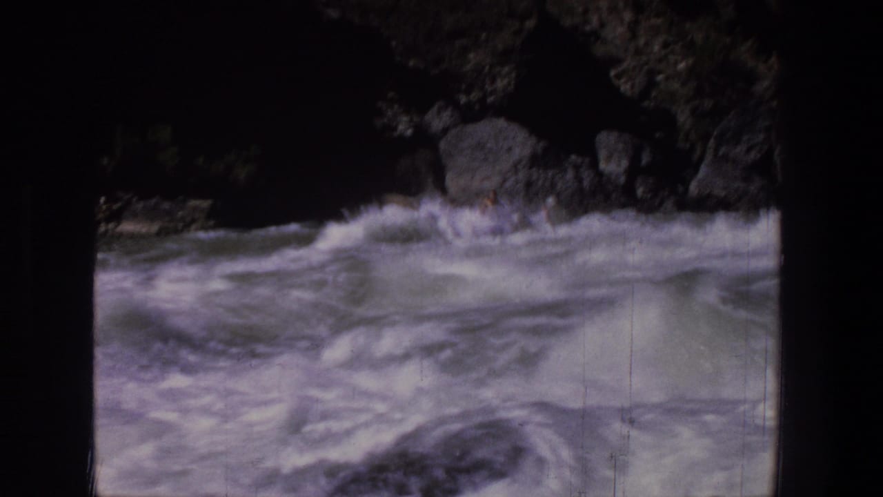 Whitewater rapids rush through a rocky river channel with dark film borders.