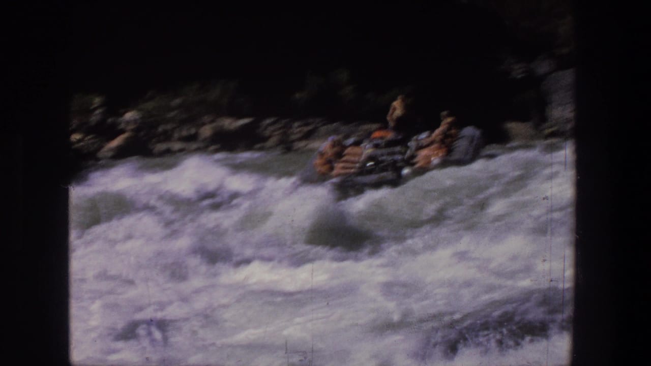 1969 Utah 8mm frame with a group in an inflatable raft entering rough whitewater, with rocks and dark canyon edges behind them.