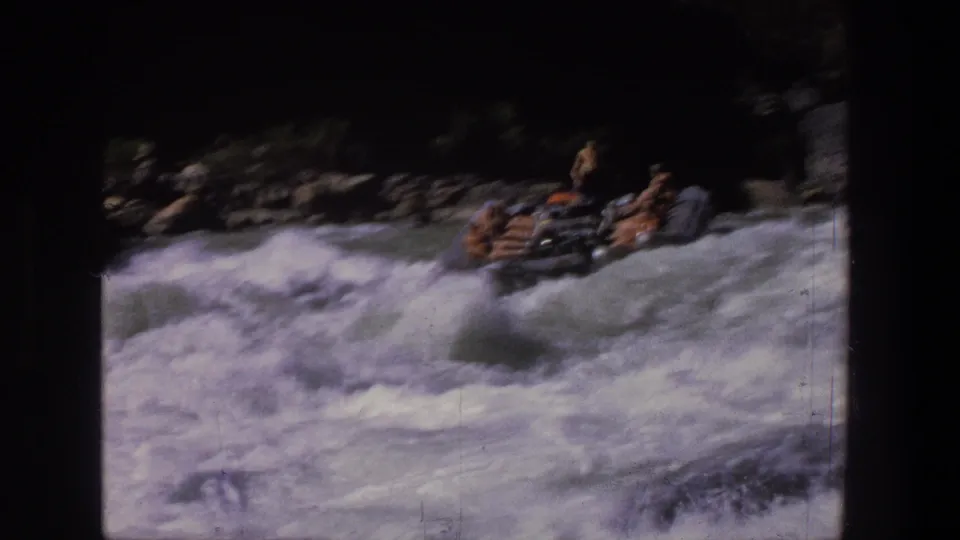 1969 Utah 8mm frame with a group in an inflatable raft entering rough whitewater, with rocks and dark canyon edges behind them.