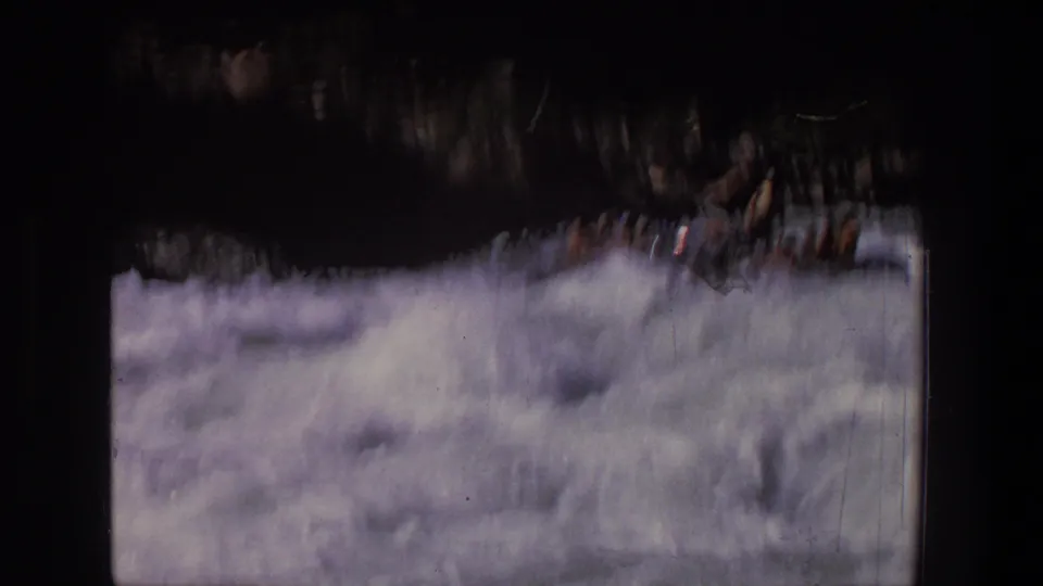 1969 Utah home-movie frame showing rafters partly hidden by spray and motion blur as the raft drops through rough water.