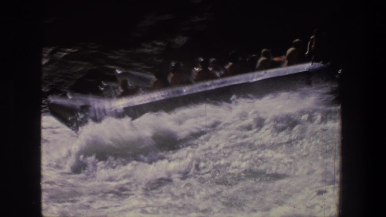 Silver raft with passengers entering foamy rapids on a dark river.