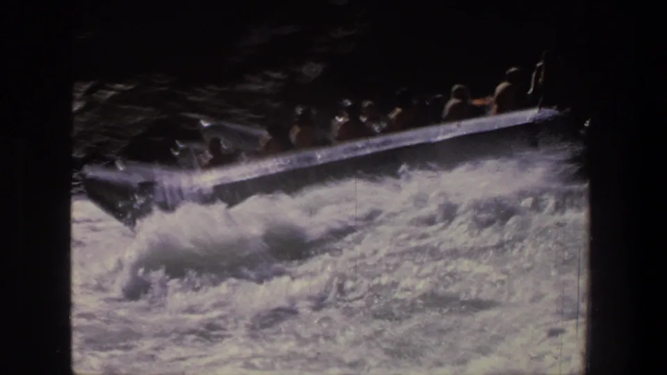 1969 Utah 8mm frame showing a silver inflatable raft with passengers riding into turbulent whitewater.