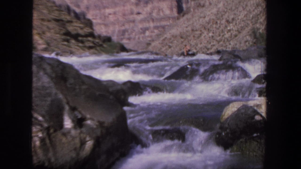 1969 Utah 8mm view of a whitewater river moving through boulders with steep canyon rock rising behind it.