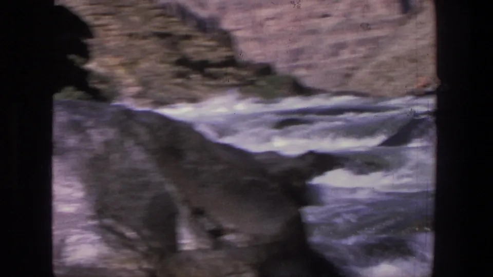 1969 Utah 8mm frame with foamy rapids, dark boulders, and a softly focused canyon wall in the background.