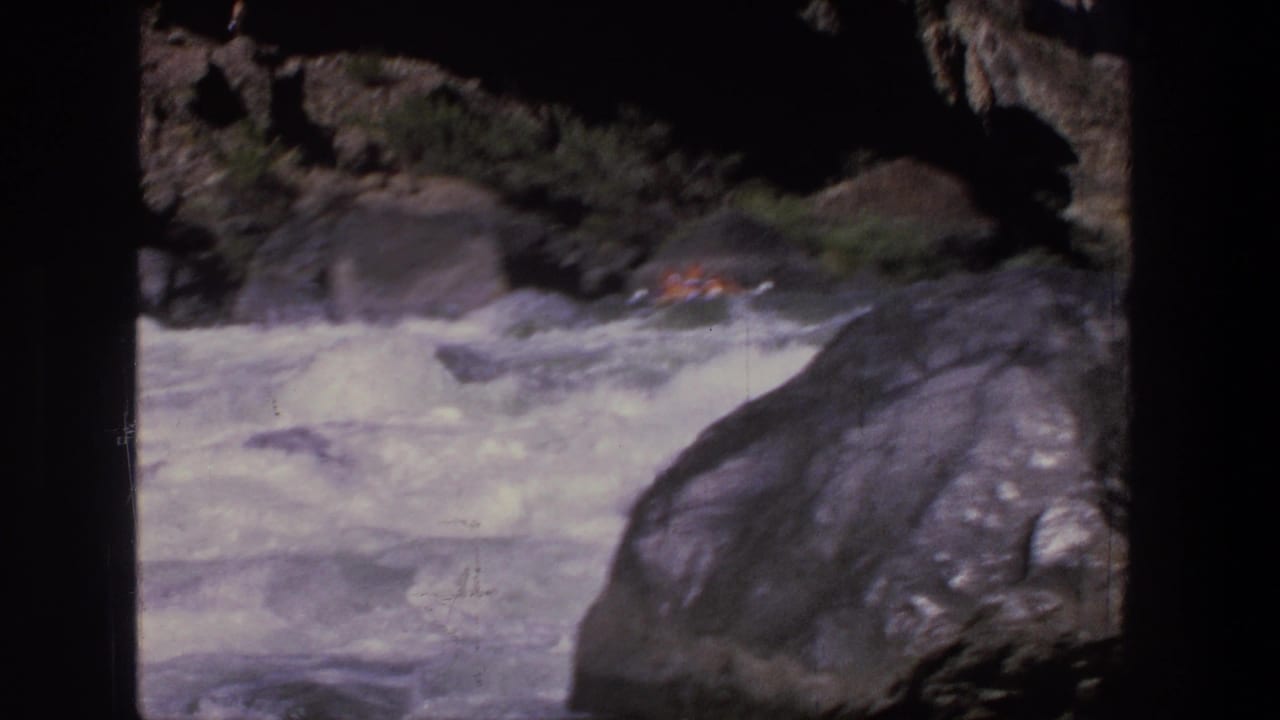 Whitewater rapids run past large rocks with a small raft visible upstream.