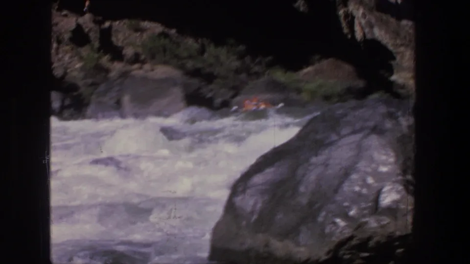 Whitewater moves through a rocky Utah canyon as a small inflatable raft appears near boulders in 1969 8mm footage.
