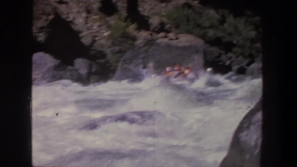 A small group in an inflatable raft continues through foamy Utah rapids framed by canyon boulders in 1969 8mm footage.