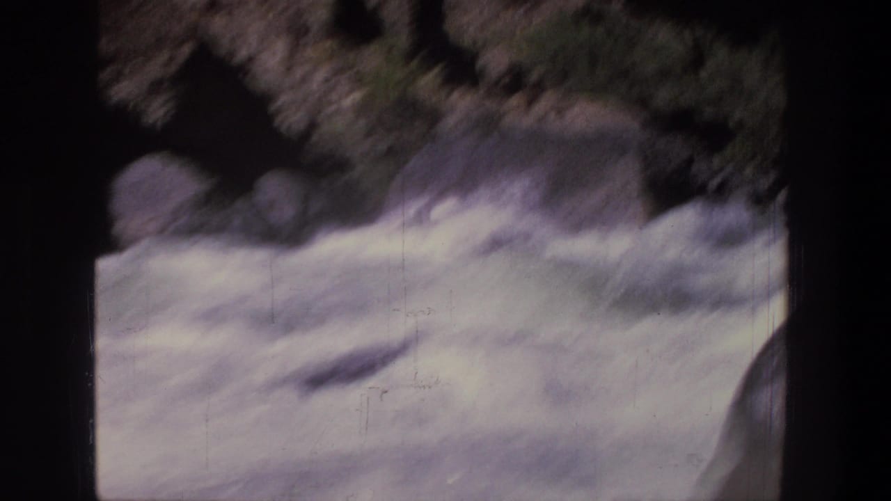 1969 Utah 8mm frame showing churning white-water rapids and dark rocky river edges from a riverside viewpoint.