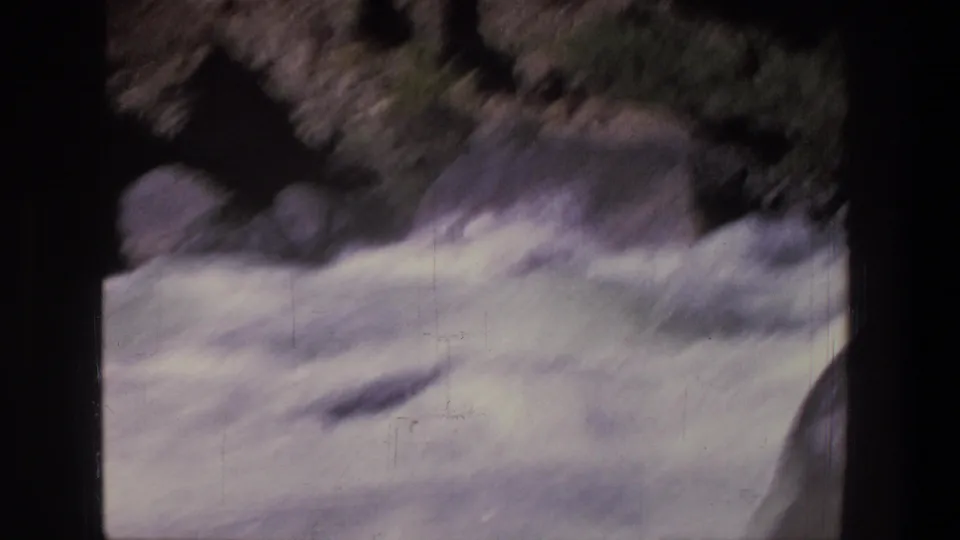 1969 Utah 8mm frame showing churning white-water rapids and dark rocky river edges from a riverside viewpoint.