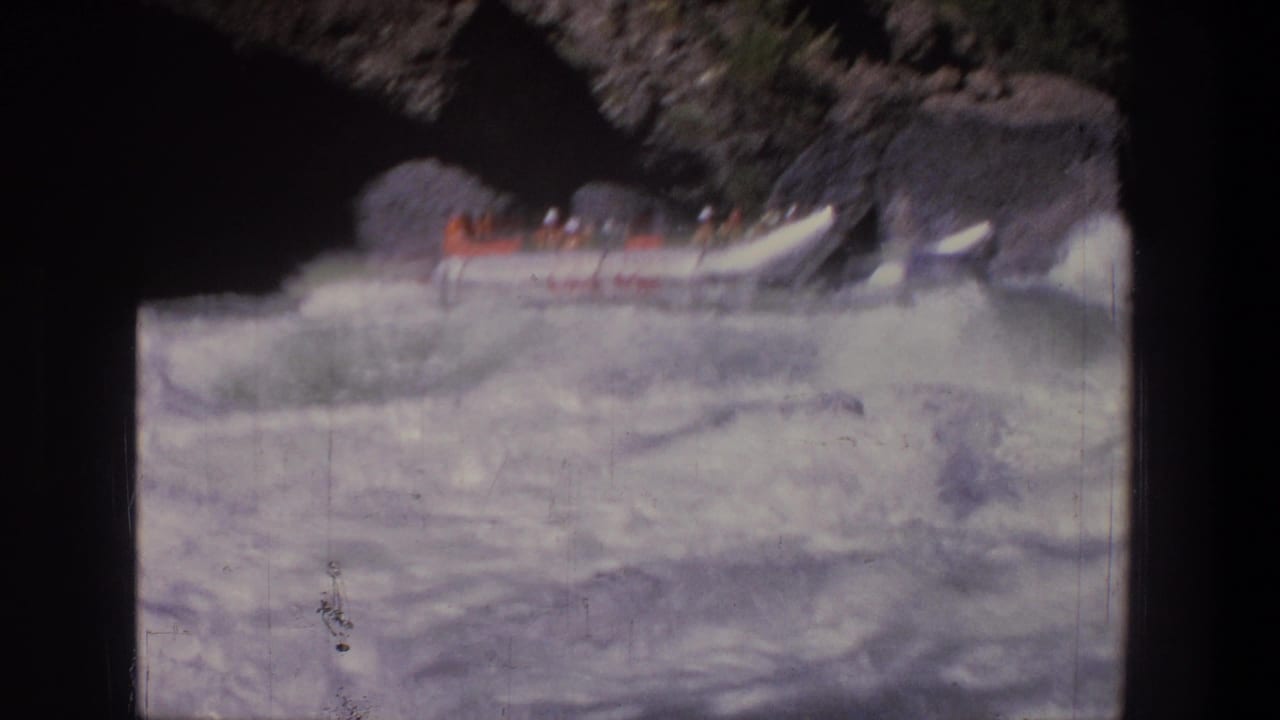 1969 Utah rafting frame with a crowded white inflatable raft moving through foamy rapids beside a rocky bank.