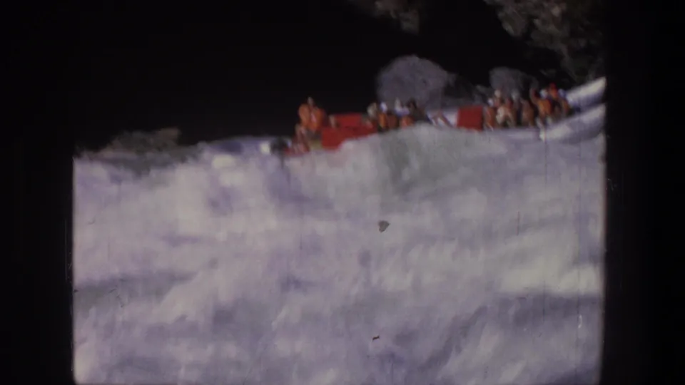 Close 1969 Utah 8mm view of passengers packed into a white raft as it rides through turbulent river water.