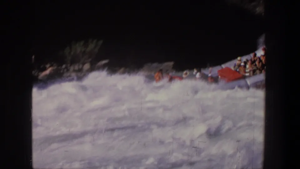 1969 Utah 8mm frame showing the raft partly framed at right as it moves through churning rapids near rocks.