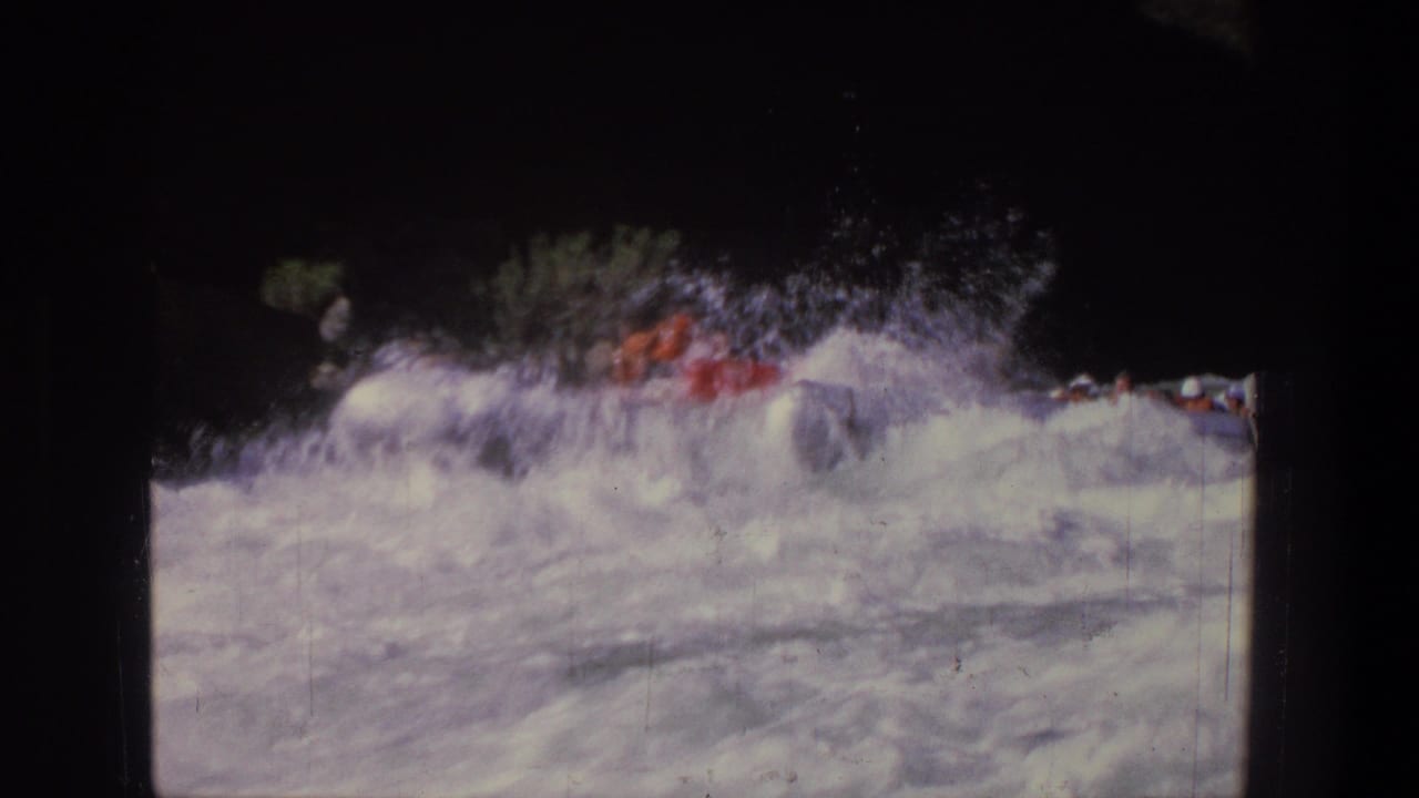 1969 Utah 8mm frame showing a red raft partly obscured by whitewater waves along a shaded riverbank.