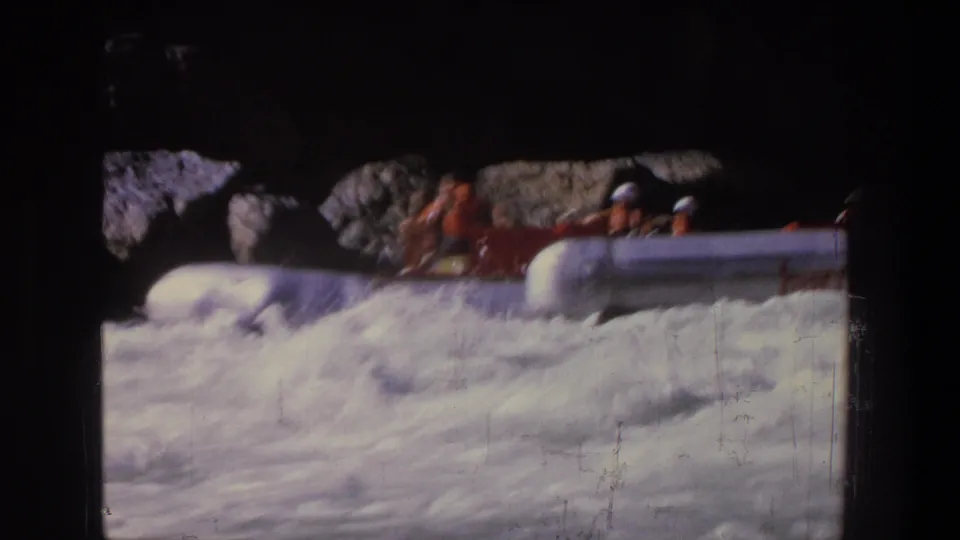 1969 Utah 8mm frame showing rafters in a red raft moving past rocks and tree shadows while whitewater fills the foreground.