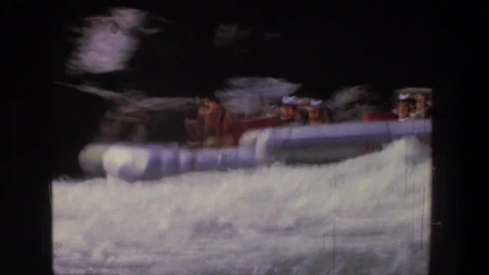 1969 Utah 8mm frame showing a red rubber raft carrying passengers into turbulent white water beside dark canyon rock.