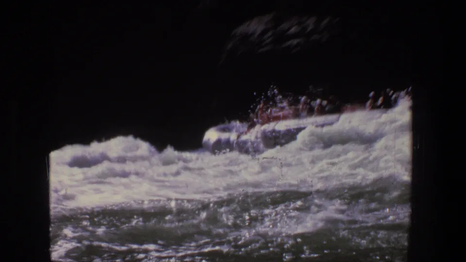 A 1969 Utah 8mm frame shows the red raft partly hidden by breaking rapids, with passengers clustered inside.