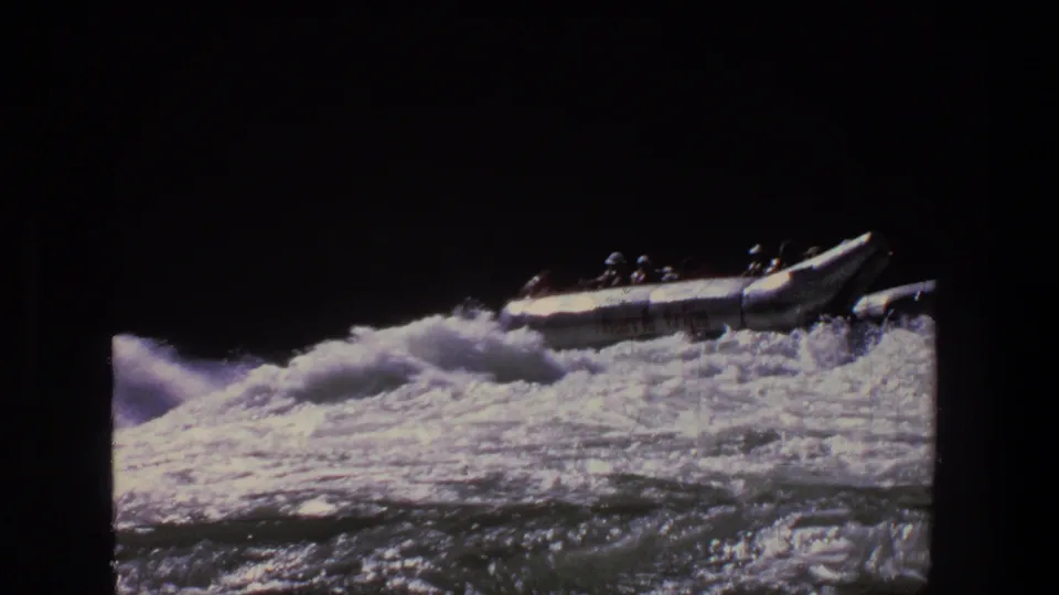 1969 Utah home-movie frame with the raft farther across the rapids, passengers silhouetted against foaming water.