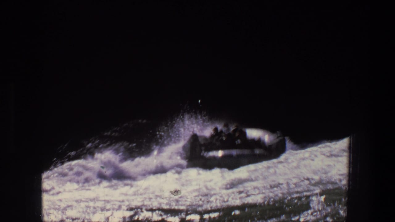 Small raft rides through churning rapids with spray rising behind it.