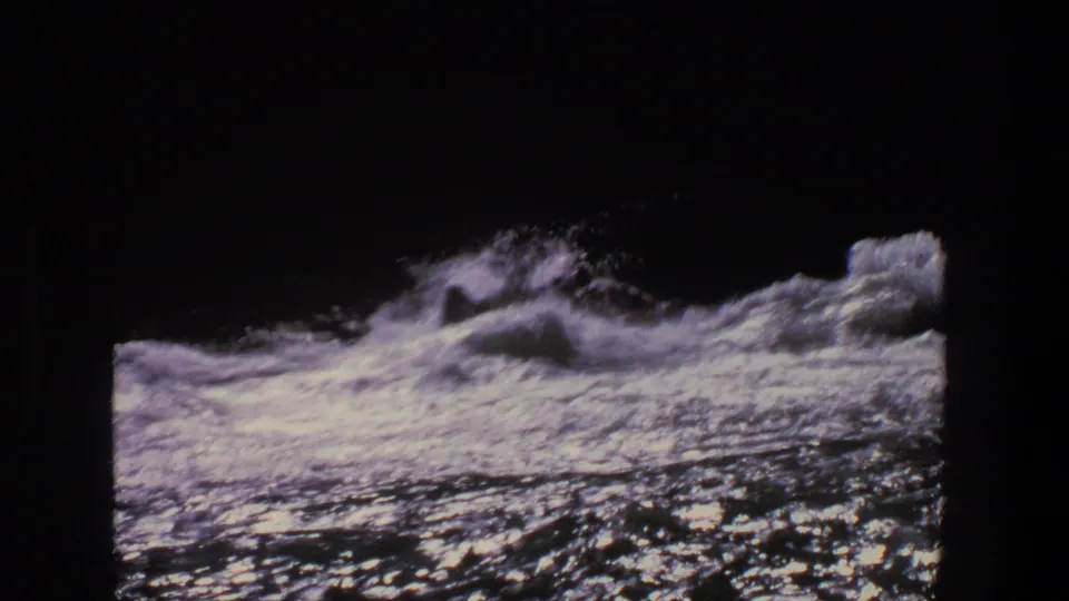 Rough whitewater dominates the 8mm frame, with a fragment of the inflatable raft near the right edge.
