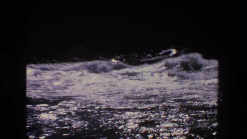 A dark inflatable raft with silhouetted people rides low through fast whitewater in this Utah 1969 home-movie frame.