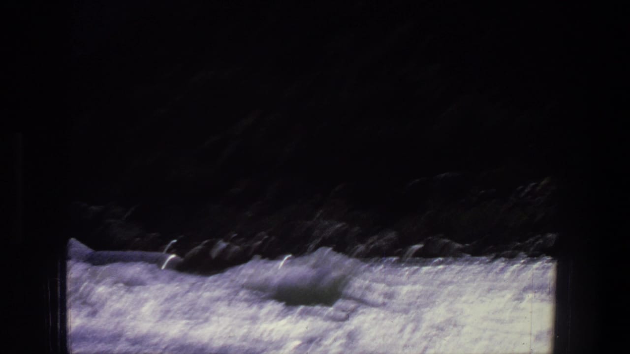 Small raft moving through bright whitewater beneath dark riverbank shadows.