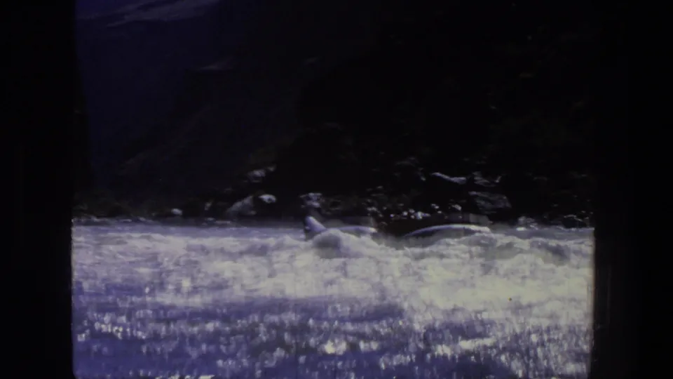 1969 Utah 8mm frame showing a small raft amid rough whitewater beside a shadowed rocky bank.