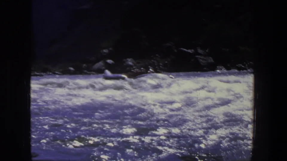 1969 Utah home-movie frame of whitewater rapids with a small raft near the shadowed riverbank.