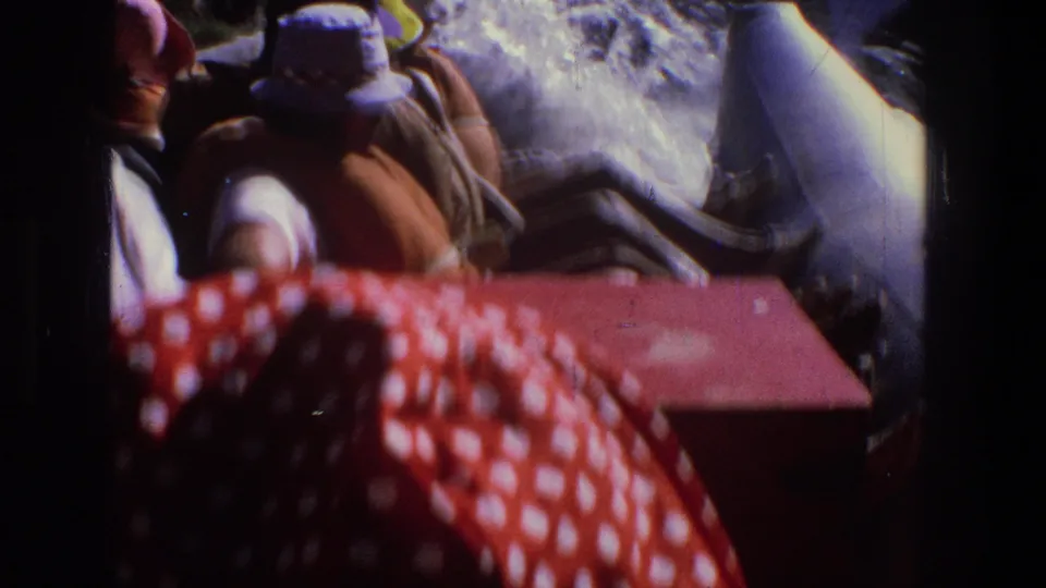 1969 Utah 8mm frame showing a group seated in a raft, with foamy river water and canyon shade around them.