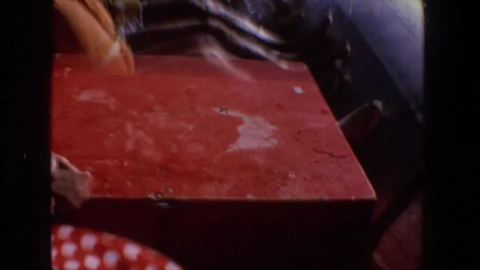 Close interior raft view with a red gear box, a passenger's hand and boot, and whitewater visible beyond the raft tube.
