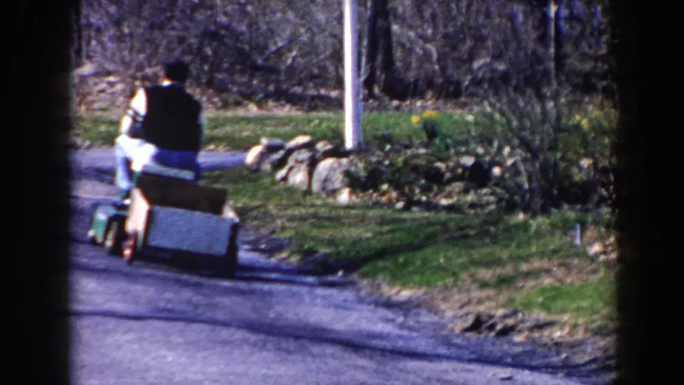 By the end of the 1964 Pequot Lakes clip, the man on the mower and his wooden cart are farther away on the residential road.