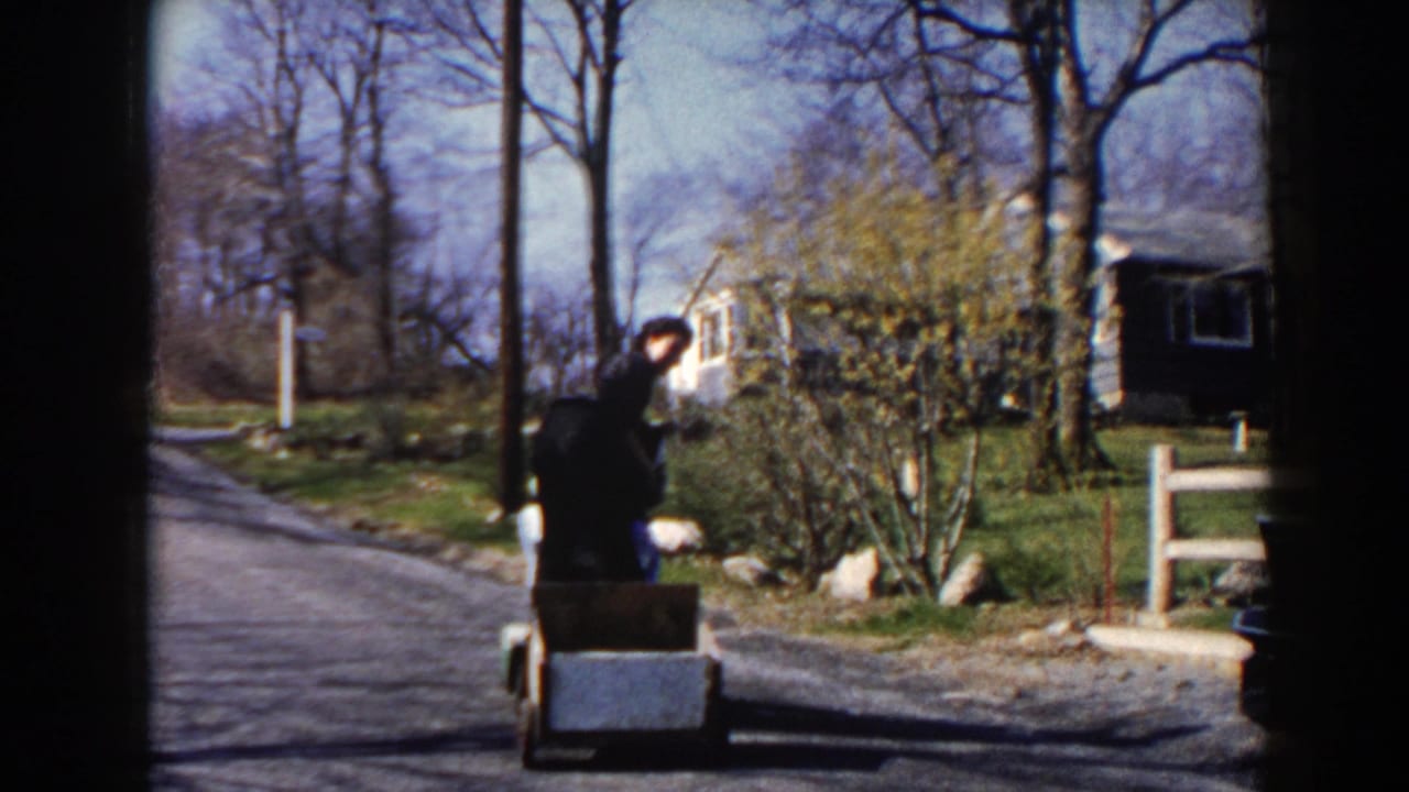 Two women ride a small motorized cart pulling a trailer on a quiet rural road.