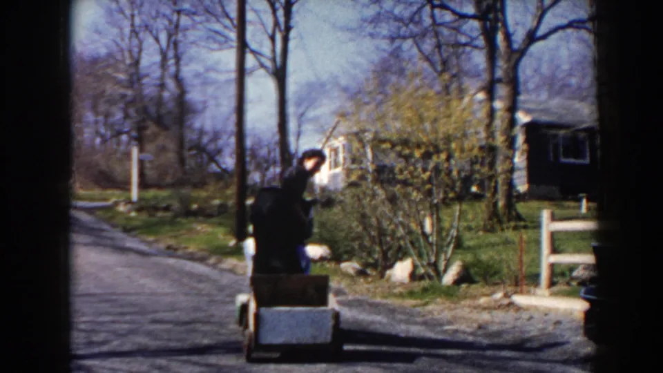 In Pequot Lakes, Minnesota, two women ride a small motorized cart with a trailer along a rural road in 1964 home-movie footage.