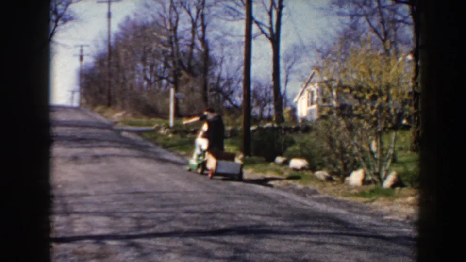 In Pequot Lakes, Minnesota, a child appears on a quiet 1964 residential road with a homemade cart, utility poles, and bare trees.