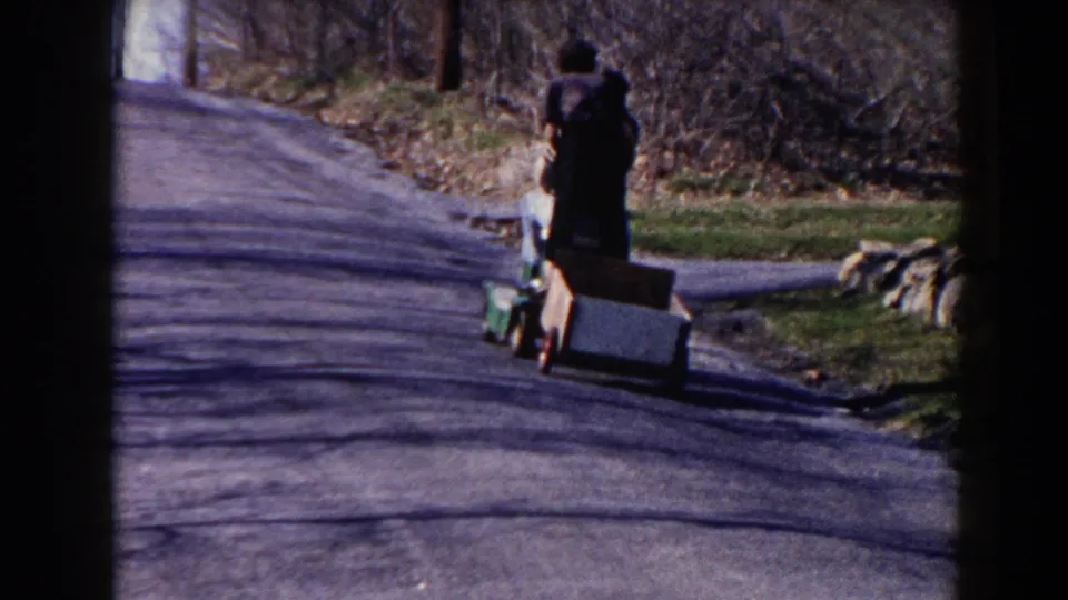 The child walks away from the camera along a Pequot Lakes road in 1964, with the homemade cart beside the grassy shoulder.