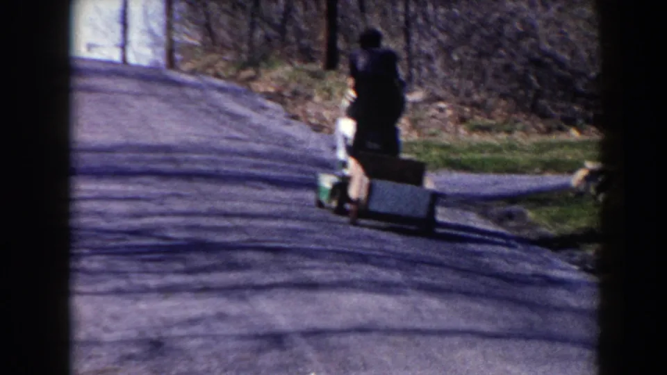 A closer 1964 home-movie view shows the child from behind with a homemade cart on the Pequot Lakes roadside.