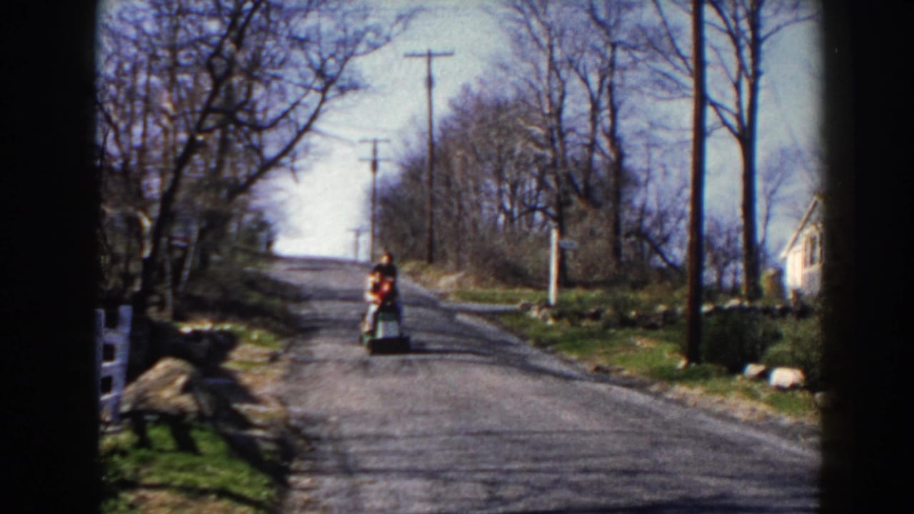 Scooter rider moves closer on the paved road with utility poles and trees in the background.