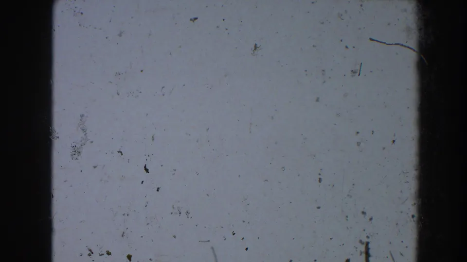 1964 Pequot Lakes 8mm frame showing blue-gray exposed film, black borders, a nearby divider, dust specks, and worn surface marks.