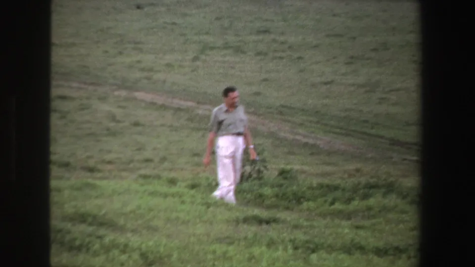 A 1969 South Africa frame shows the man moving through grass and low vegetation, with soft focus and grain from 8mm film.